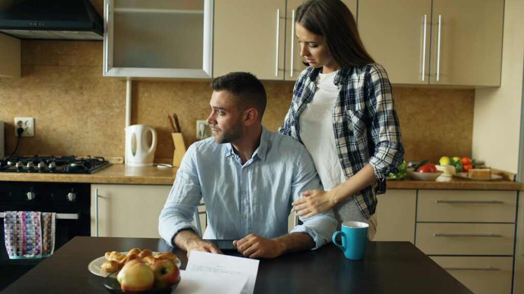 A couple reviews life insurance papers and a beneficiary form at a kitchen table.